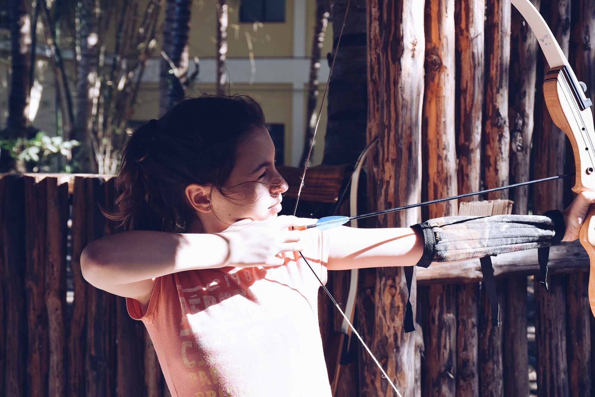 A young girl practicing archery, aiming at a target with a bow and arrow