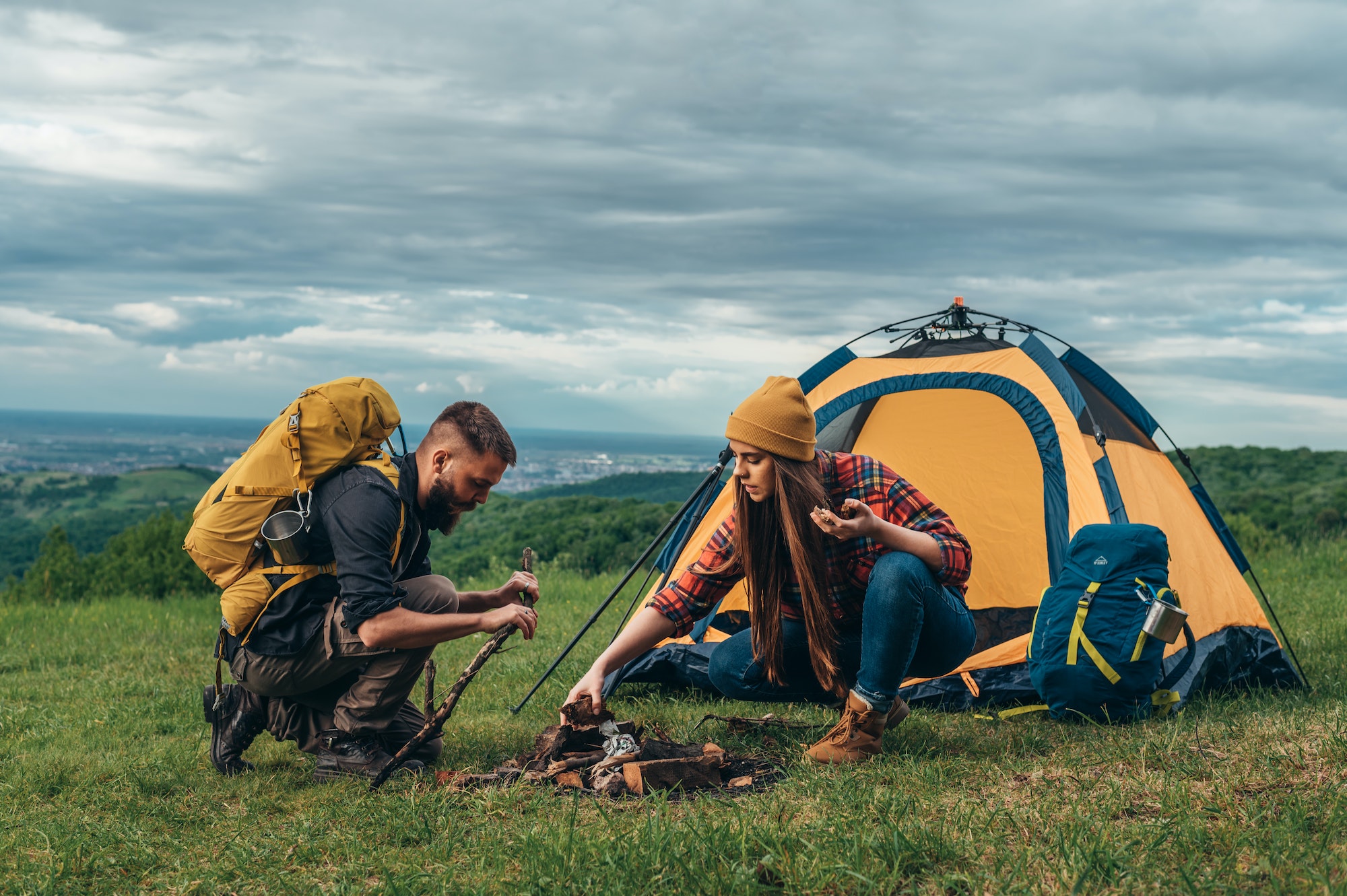 Couple of campers lighting a fire while setting up the camp tent