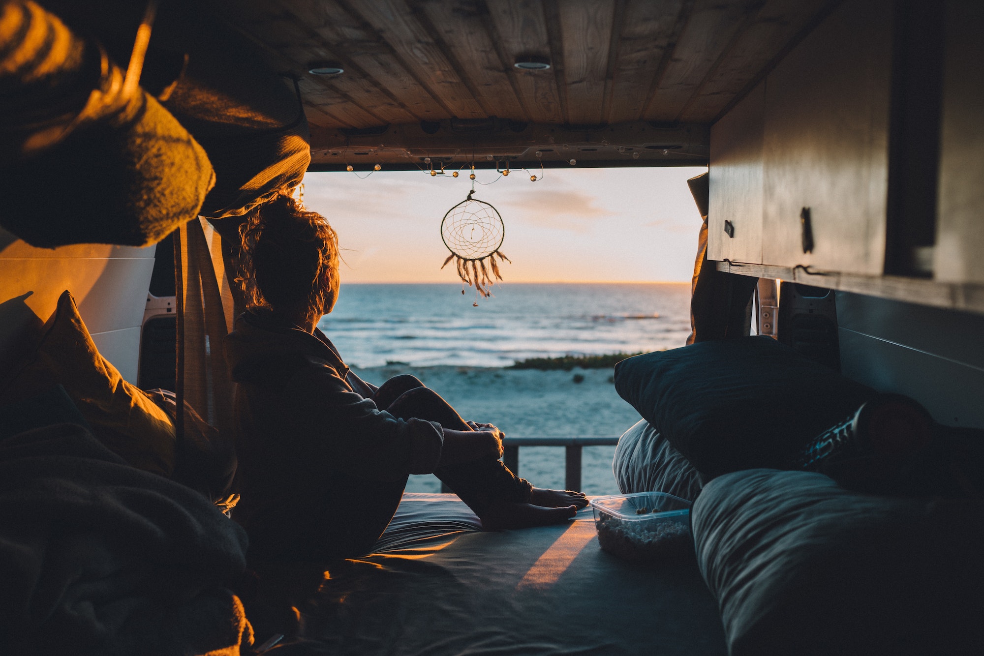 Female sitting in the van and admiring the sunset in the beach